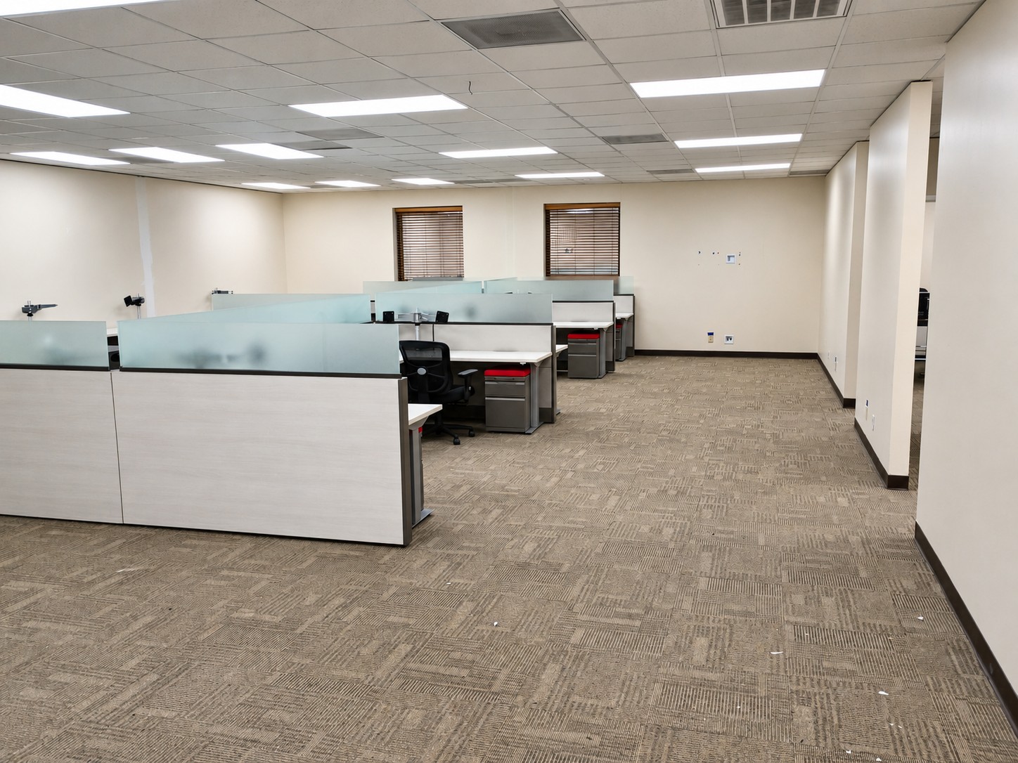 An office space with workstations, ceiling lighting, and carpet flooring.